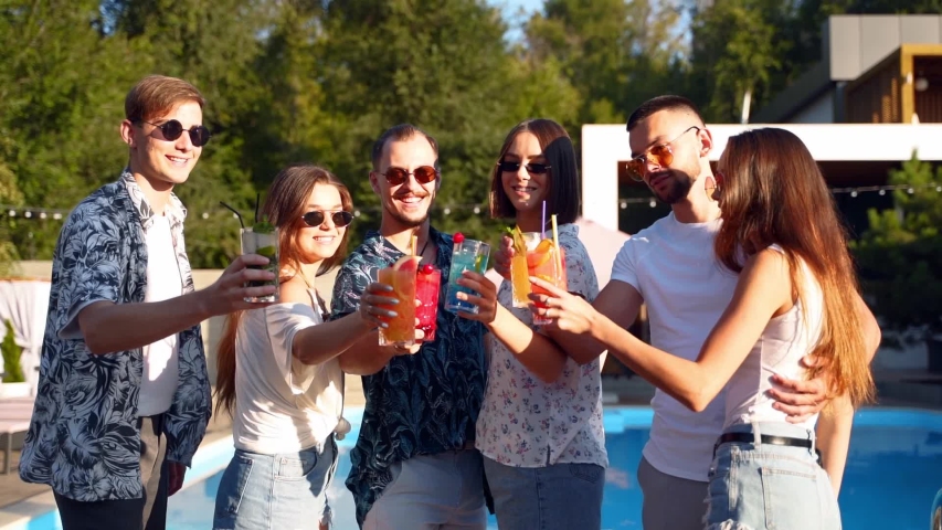 Group of friends having fun at poolside summer party clinking glasses with summer cocktails at camera near swimming pool. People toast drinking fresh juice at luxury villa on tropical vacation. | Shutterstock HD Video #1054066835