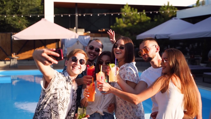 Smiling friends taking selfie with smartphone at pool party toasting with colorful cocktails by swimming pool on sunny summer day. Man taking photo at luxury villa on tropical vacation. Slow motion. | Shutterstock HD Video #1054066850
