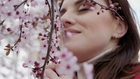 Young pretty smiling caucasian woman standing near blooming spring tree.