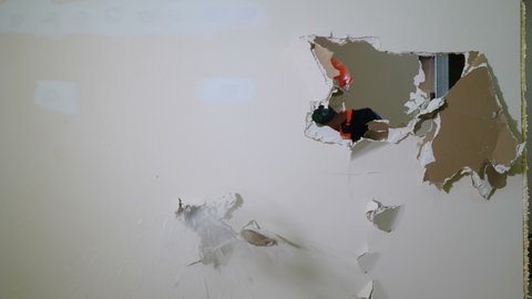 Worker in uniform destroys inner wall sledge hammer. Demolition work and rearrangement concept. Wall made of gypsum cardboard being destroyed. 4 k video
