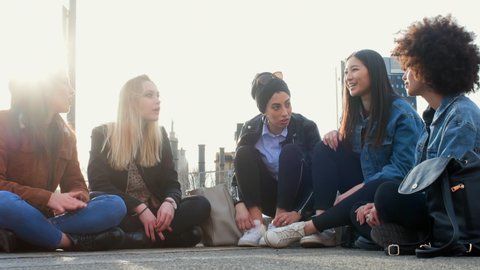 A group of girls, young women, female friends sitting on the ground talking and laughing.