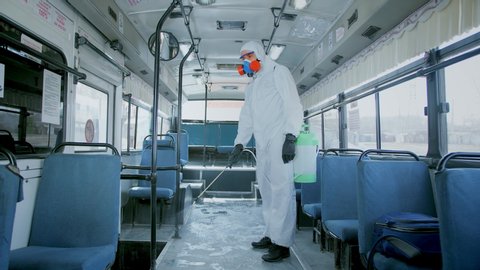 Man Disinfect Bus. Covid-19. Corona Virus Disinfection Transport. Antiseptic Sanitizer. Coronavirus Disinfectant. Worker Wear White Uniform Suit. Protect Mask covid 19. Spray Disinfecter corona virus.