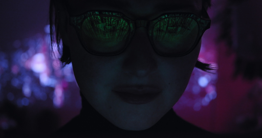 Pretty female hacker in glasses working night on computer in cyber security center filled with digital display screens. Binary code matrix source and cyberspace symbols reflection on her face. Closeup Royalty-Free Stock Footage #1054086665