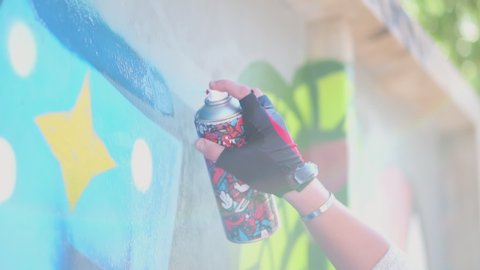 Beautiful Young Girl making a colorful graffiti with aerosol spray on urban street wall at summer. Creative art. Talented female hipster student drawing picture. Freedom, lifestyle, culture concept.