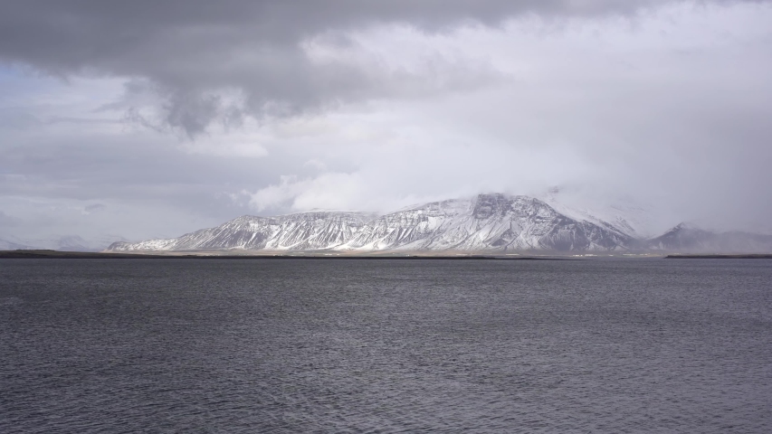 A snow-covered mountain on the Atlantic coast in Iceland. View from the other side, or from the sea. Cloudy weather, dense clouds.