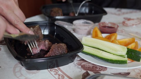 Food delivery service, couple at home eating steak mignon in lunch box containers, delivered from restaurant.
