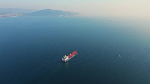 Aerial view, ultra large cargo or container ship at sea leaves port at sunset. Top down drone footage of tanker. Concept of transport logistics, maritime.