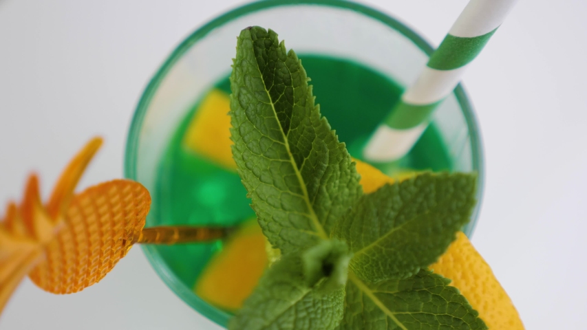 Festive green cocktail in a glass with lime, lemon and mint. Cooling summer drink rotate over white background. Top view.
