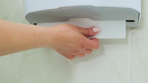 Close up of woman hands pulling tissues from white plastic box in dental clinic. White paper towel dispenser on the wall. Health care and prevention concept.