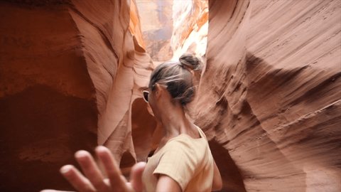 SLOW MOTION: Young woman running inside narrow canyon in the desert, waving her hand inviting her companion to follow her. Tracking shot, pov couple enjoying hike inside Antelope Canyon, USA