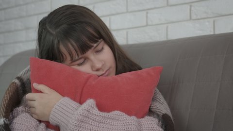 Child sleep with the pillow. Pretty girl in a warm clothes embrace a red pillow in the bed in the room.