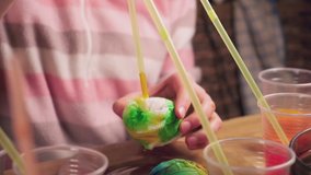 Close up video of hands of children using dye and painting on white boiled eggs while preparing for Easter, 4K UHD video