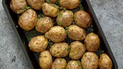 Oven baked whole potatoes with seasoning and herbs in metalic tray. Roasted potatoes in jackets. Top view. Close up.