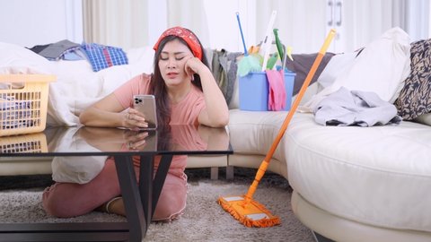 House maid looks lazy while using a mobile phone with untidy living room at home. Shot in 4k resolution
