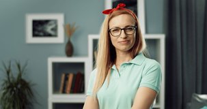 Attractive woman with blond hair smiling while spraying detergent in front of camera. Mature housewife in glasses and rubber gloves taking fun during cleaning time at home.