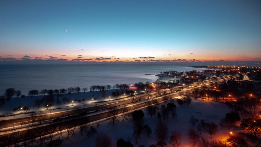 Beautiful vertically panning up aerial morning sunrise timelapse of the Chicago Lakefront along Lake Michigan with traffic passing by on Lake Shore Drive as the sun comes up over clouds on the horizon.