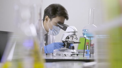 Asian scientist doing some research and looking through a microscope in laboratory.