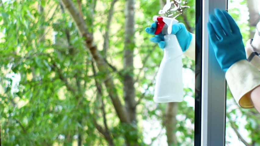 Woman in blue gloves spraying a special liquid in the form of antibacterial foam onto the glass window. domestic cleaning. | Shutterstock HD Video #1054117616