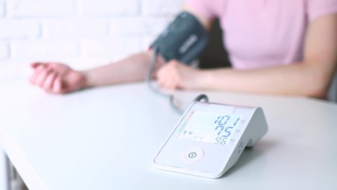 Woman hand and white electric tonometer on table for measuring blood pressure Healthy concept. Measurement of pressure and pulse. Hypertension and hypotension