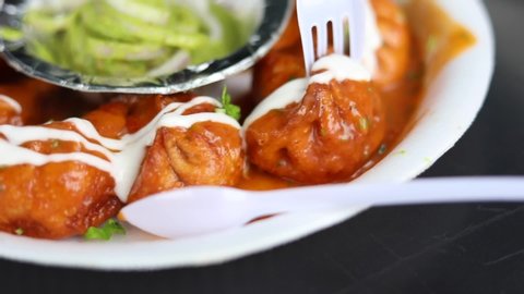 Closeup shot of gravy butter chicken momos topped with mayonnaise dressing and green mint chutney, served on a paper plate.