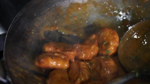Tossing chicken momos in red spicy gravy with chilly in an Indian style pot or kadhai.