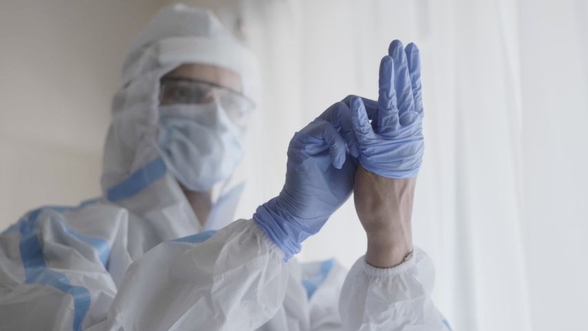 A close up shot of a doctor or healthcare worker in personal protective kit preparing and wearing hand gloves in the interior hospital or clinic setup amid Coronavirus or COVID 19 epidemic or pandemic Royalty-Free Stock Footage #1054123877