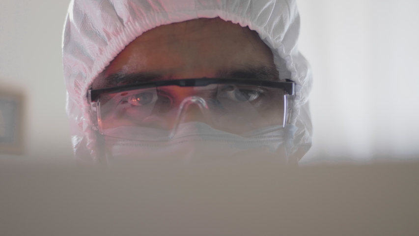 Ambulance lights flashing on the eyes of the doctor or healthcare worker working on a laptop in emergency room of the hospital wearing personal protective kit amid Coronavirus or COVID 19 epidemic