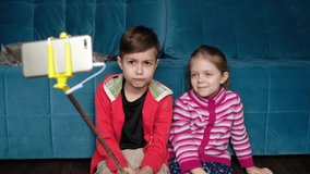 Boy and girl are photographed on the phone. Children use a selfie stick.