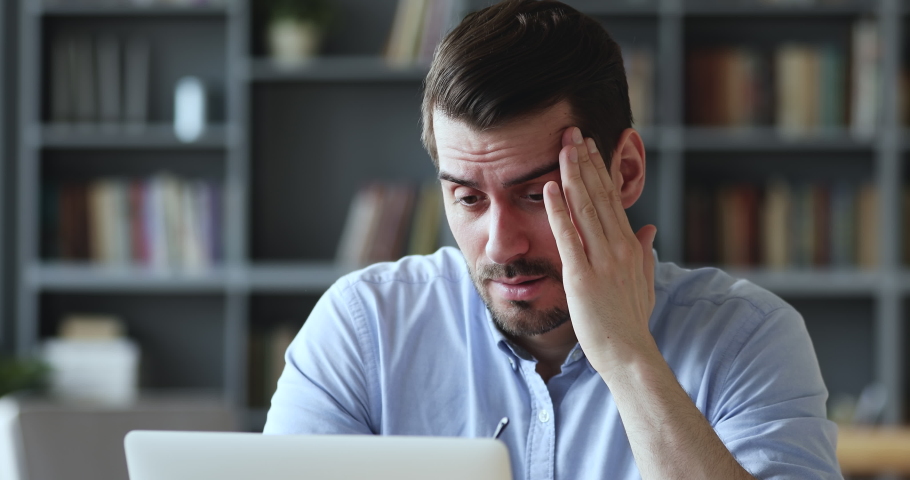 Stressed young man in glasses suffering from muscles tension, having painful head feelings due to computer overwork or sedentary working lifestyle. Tired employee overwhelmed with tasks in office. | Shutterstock HD Video #1054130741