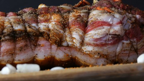 Fresh juicy piece of raw meat pork steak or bacon with seasonings of pepper, garlic, carrots in rustic style rewound with baking threads in the oven salted and spiced, garnished on wooden background.