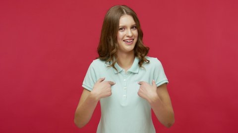 Wow, you choose me? Surprised young brunette woman in polo t-shirt pointing herself and looking with amazement, shocked about success, unbelievable achievement. studio shot isolated on red background