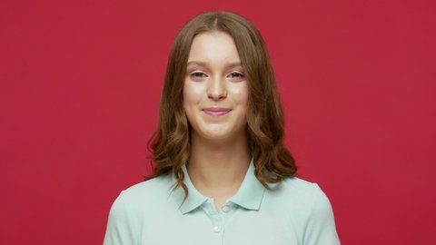 Playful happy contented brunette woman in polo t-shirt blinking eye, looking at camera with toothy smile, winking and flirting, expressing optimism. indoor studio shot isolated on red background
