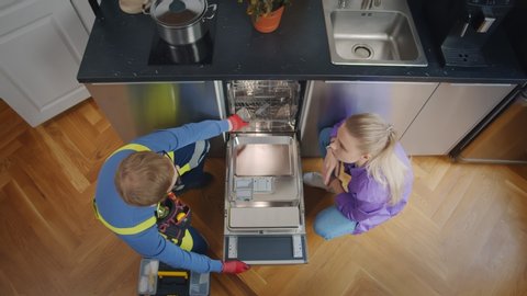 Top view of serviceman installing new dishwasher and shaking hands with female customer. Housewife and plumber fixing dishwashing machine in modern kitchen