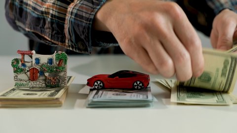 man hands counting us dollar banknotes. counting money for new purchases. saving money for car, house, travels. savings concept. A small house, car and  shell lies on a table of thousand dollars
