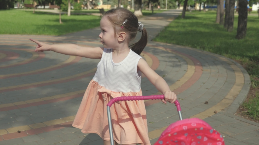 little girl walks in the park with a stroller and a teddy bear. A kid on the street with his favorite toy. the child plays in playground. healthy childhood concept