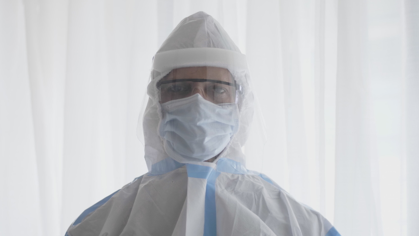 A close shot of a confident doctor or healthcare worker in a personal protective kit standing in a  hospital or clinic and looking into the camera amid coronavirus or COVID 19 epidemic or pandemic 