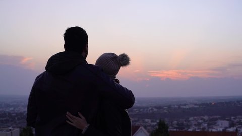 Young cute couple on romantic date hugging and looking at panoramic city view and sunset