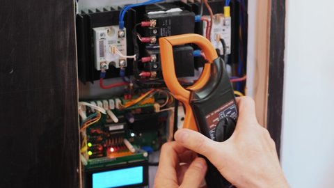 Electricians hands testing current  electric in control panel. Electrician engineer work  tester measuring  voltage and current of power electric line in electical cabinet control.