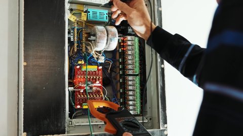 Electricians hands testing current  electric in control panel. Electrician engineer work  tester measuring  voltage and current of power electric line in electical cabinet control.

