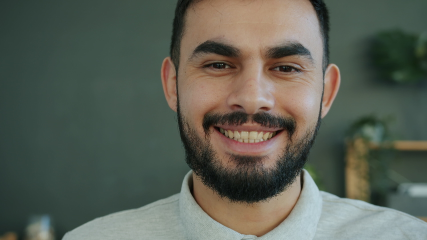 Close-up portrait of attractive bearded Arab man smiling indoors at home looking at camera with happy face. Positive emotions and modern people concept. Royalty-Free Stock Footage #1054148594