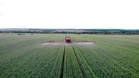 Aerial view of the tractor that irrigates the green field. Chemical treatment of the field with pesticides and protection against insects of rodents, parasites and pests