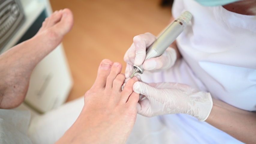 Hardware medical pedicure with nail file drill apparatus. Patient on pedicure treatment with pediatrician chiropodist. Foot peeling treatment at spa with a special device. Clinic of Podiatry Podology. Royalty-Free Stock Footage #1054153076