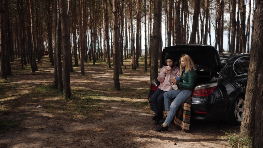 Two girlfriends on picnic in the woods at the car. Emotional conversation