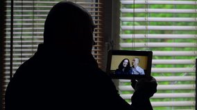 Silhouette of a bald man and his friends communicate via video chat on a tablet. Self-isolation, quarantine, the concept of a pandemic