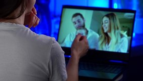 A portrait of a dark-haired woman, she communicates on a laptop on a video call and claps her hands, on the screen she shows a family: a man, a woman and a little girl. Video calls in quarantine.