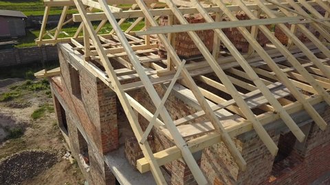 Aerial view of unfinished brick house with wooden roof frame structure under construction.