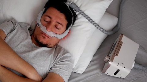 Eskisehir / Turkey - 01 11 2020: Close-up of healthy young adult man wearing under the nose nasal mask ( CPAP mask ) and using CPAP machine for sleeping smooth without snoring.