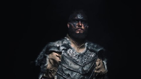 The brutal Viking cast his axe on his shoulder and shouts into the camera. A Scandinavian warrior in war paint puts an axe on his shoulder and shouts frighteningly at the camera