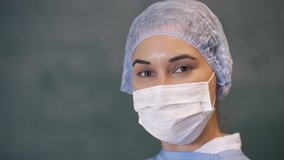 Female doctor looking at camera smiling with mask and bonnet. Slow motion 4K video.