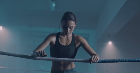 Caucasian female beautiful boxer leaning on ring rope and feeling herself tired and bad. Attractive sportswoman having pain in muscles. Body ache after sport training.